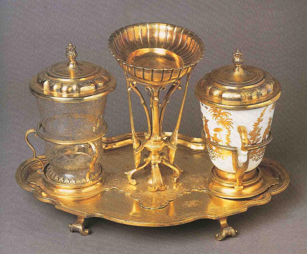 Servizio  “solitaire” con  tazza biansata decorata a cineserie e 
bicchiere di cristallo inciso su supporto in metallo dorato 
Meissen, periodo Höroldt, 1725 circa
Metallo punzonato “EA” (Augsburg, Elias Adam, 1725) 
Porcellana dura dipinta in monocromia oro 
Astuccio in pelle e metallo; interno in velluto verde
